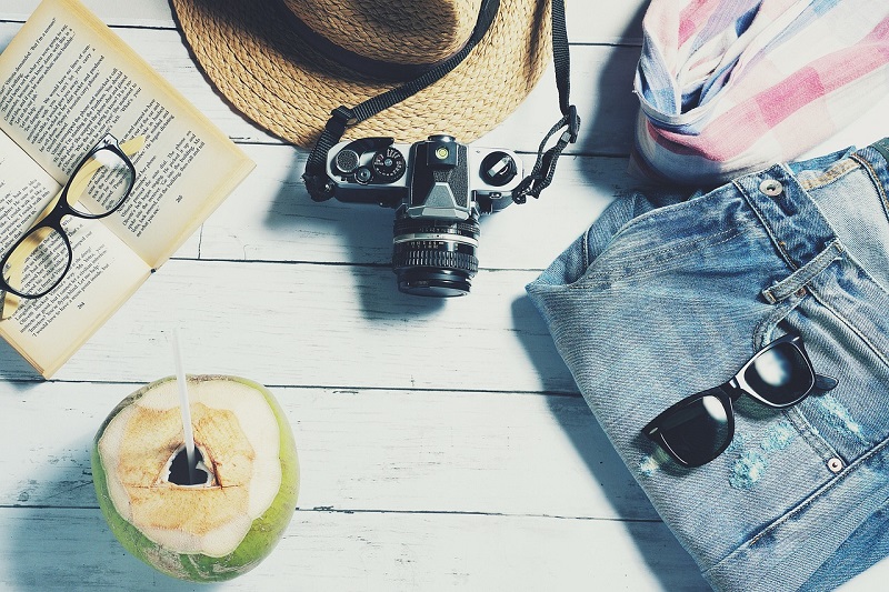 Must Have Summer Vacation Items View of a Camera, Hat, Coconut, and Clothing Laid Out Before Packing