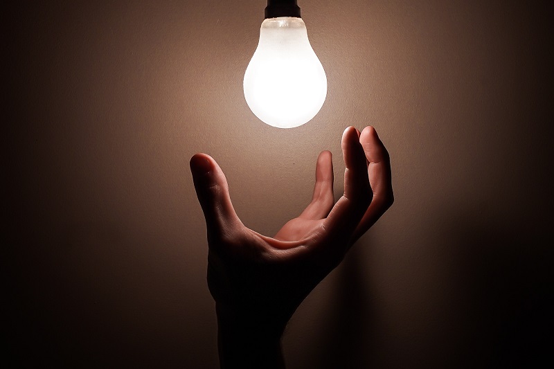 Smart Lights That Don't Require Hubs a Hand Reaching Up Toward a Light Bulb That is Turned on in a Dark Room