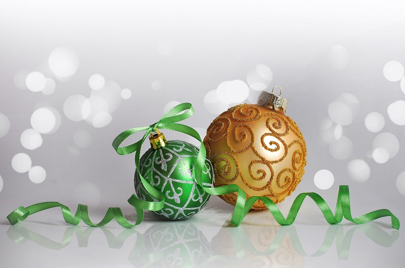 Socially Distanced Holiday Party Ideas a Green Ornament and a Gold Ornament on a White Surface